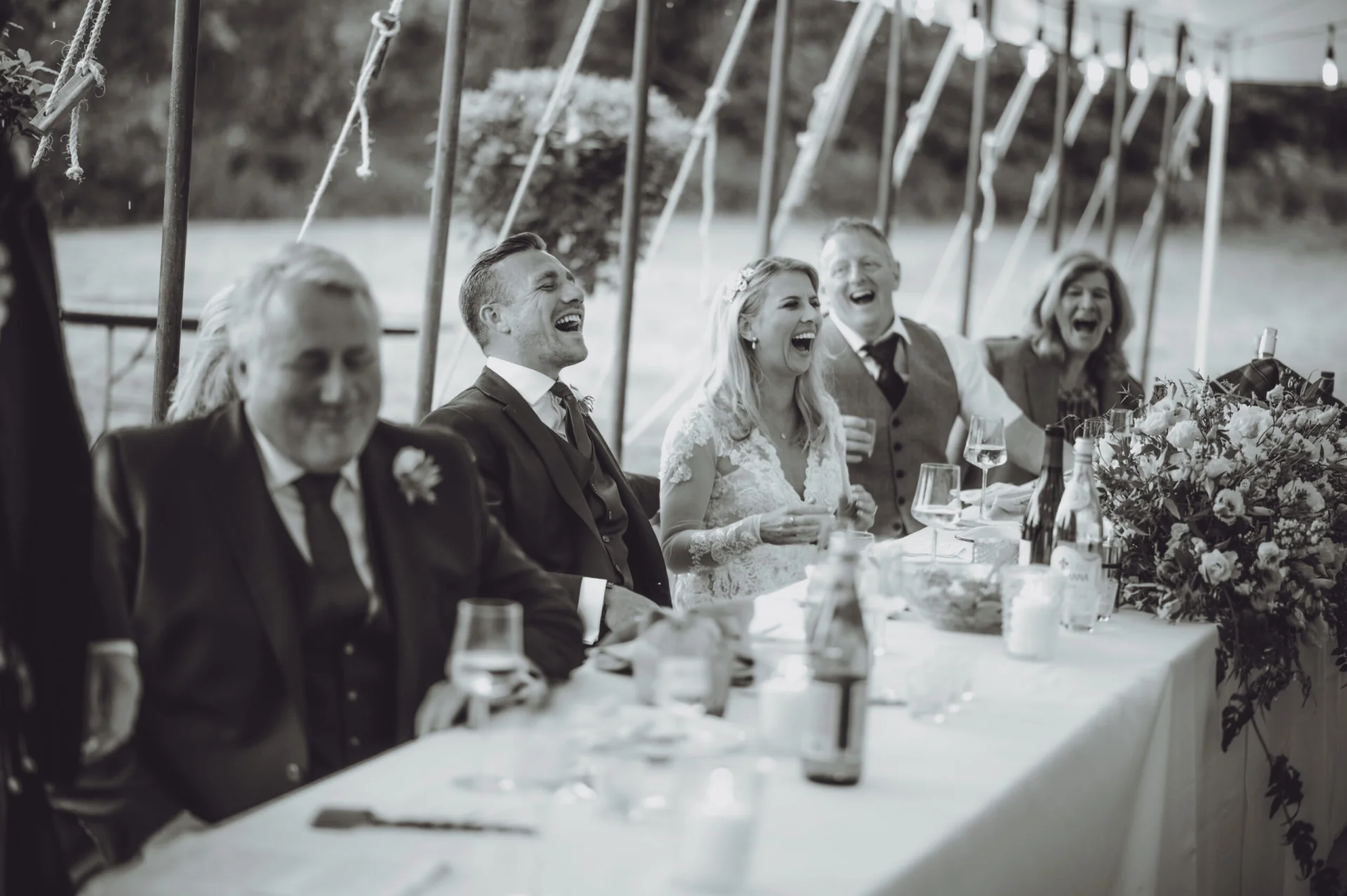 A black and white photo of a group of people laughing at a table. (listing)