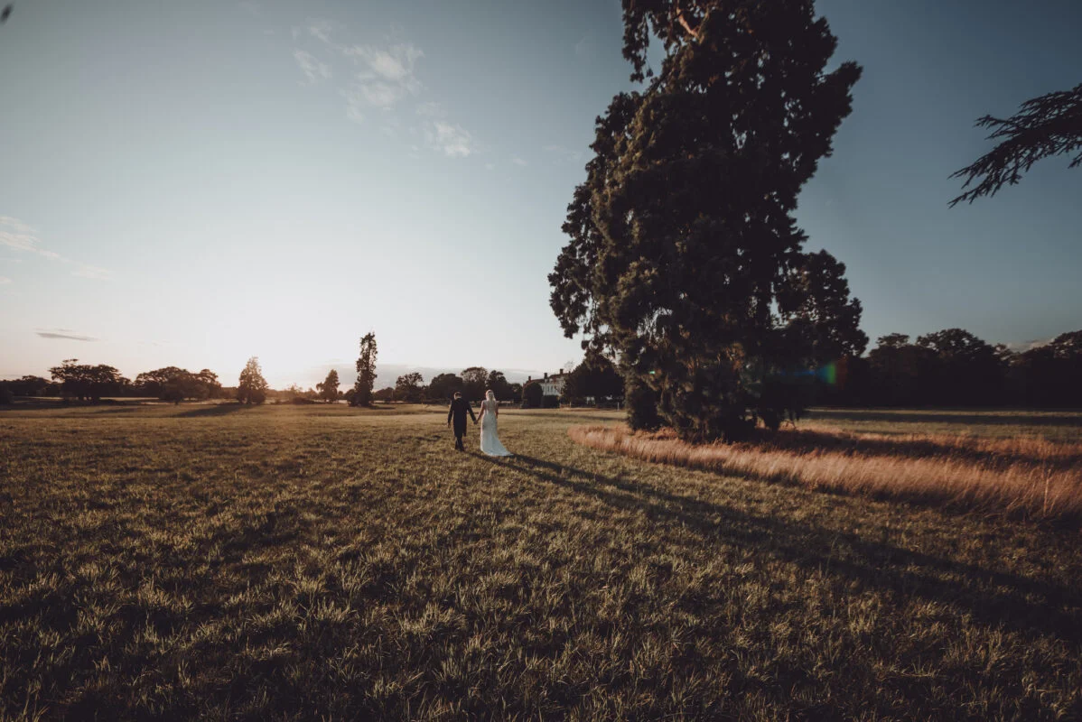 A bride and groom walking in a field at sunset.