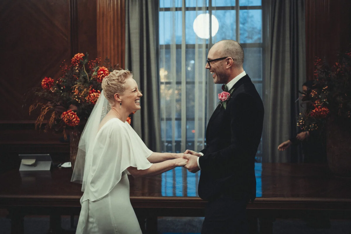 A bride and groom standing in front of a large window.
