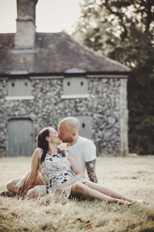 A couple kissing in front of a stone house.