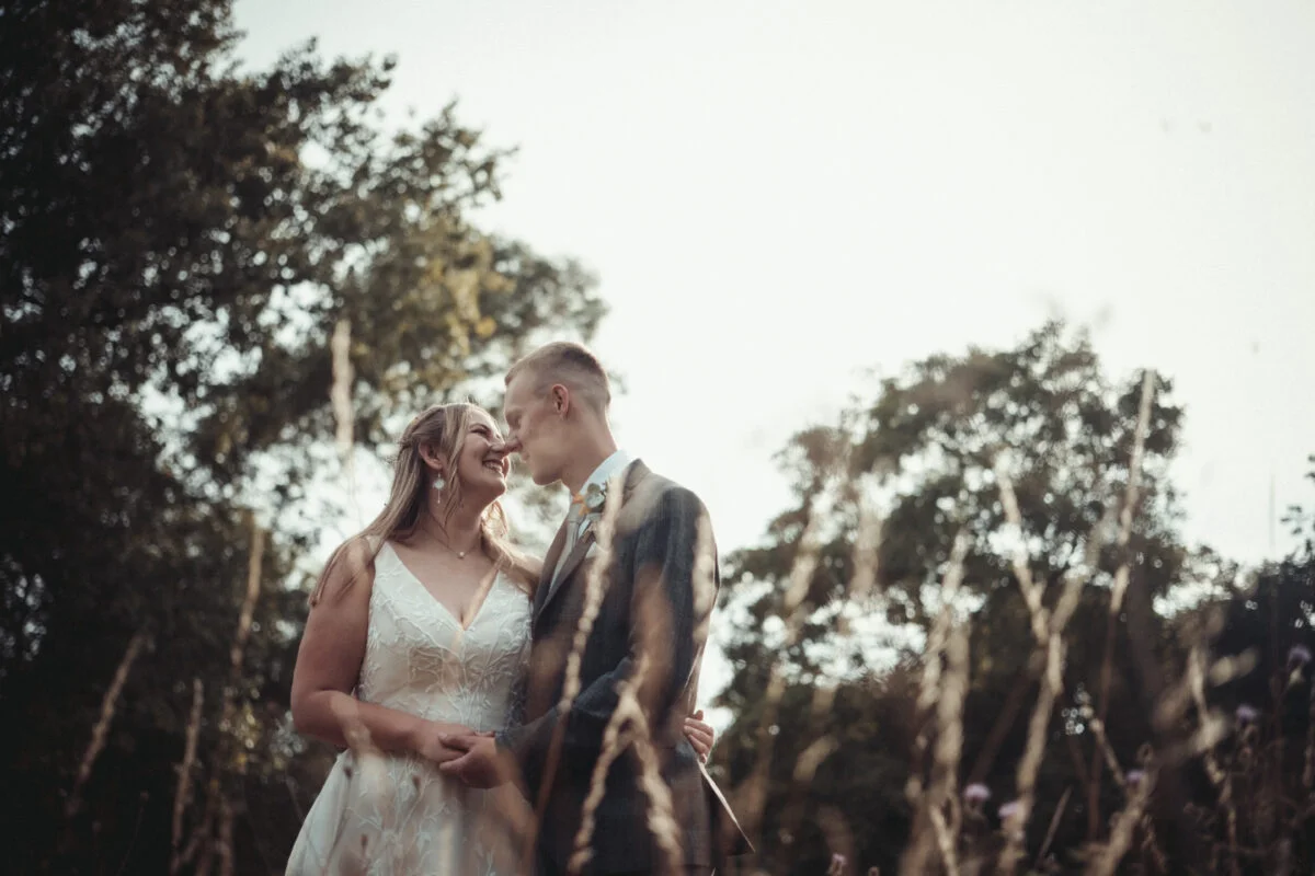 A bride and groom kissing in tall grass.