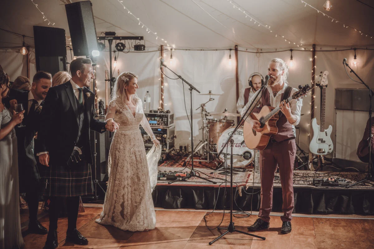 A bride and groom singing at a wedding reception in a tent.
