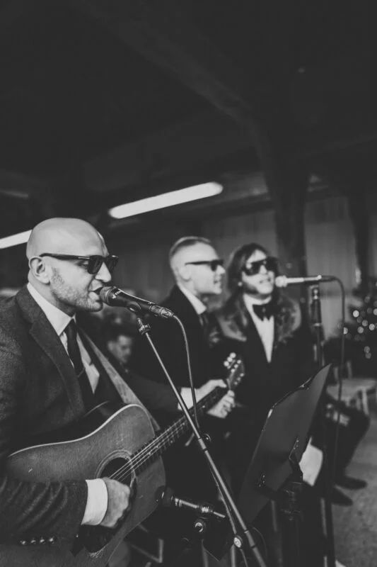 A black and white photo of a man in a suit playing an acoustic guitar.
