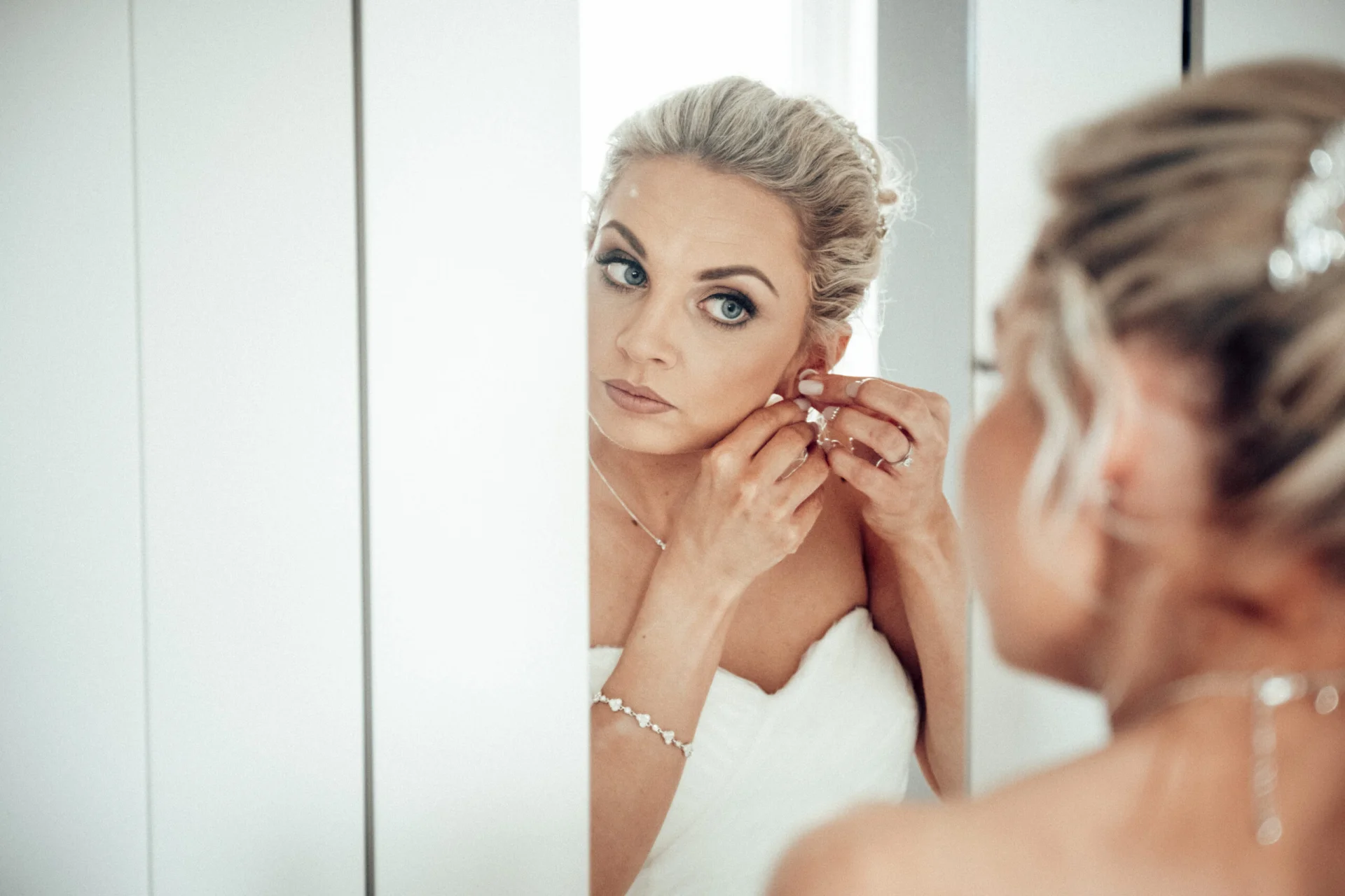 A bride putting on her wedding earring in front of a mirror. (listing)