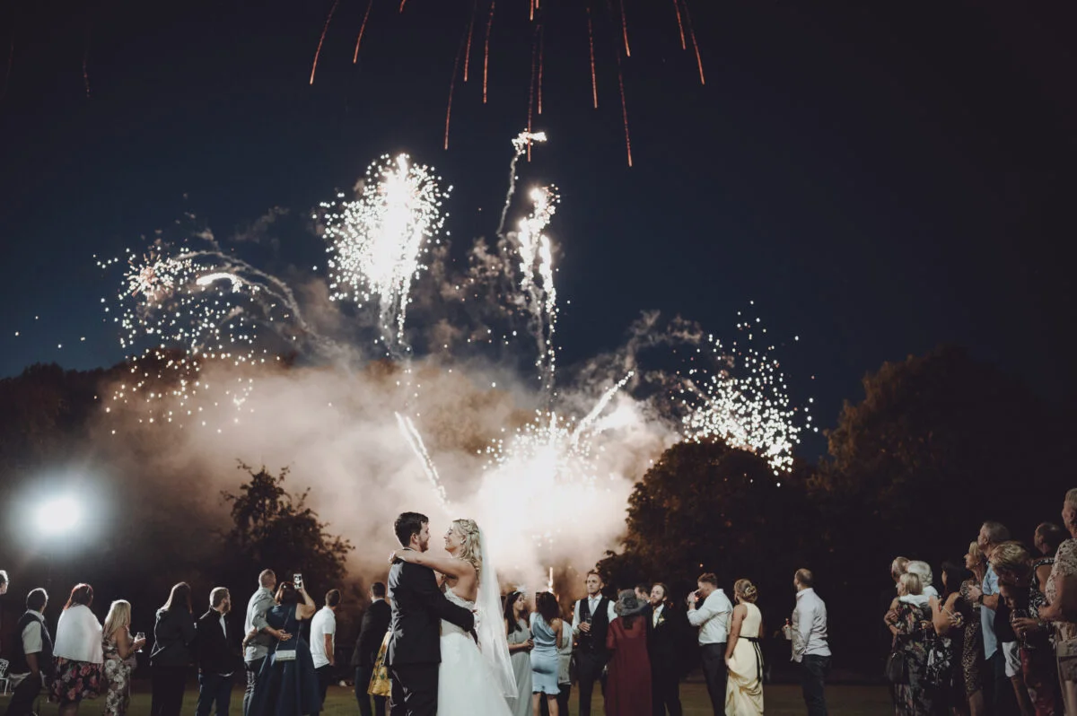 A bride and groom kissing in front of a firework display.