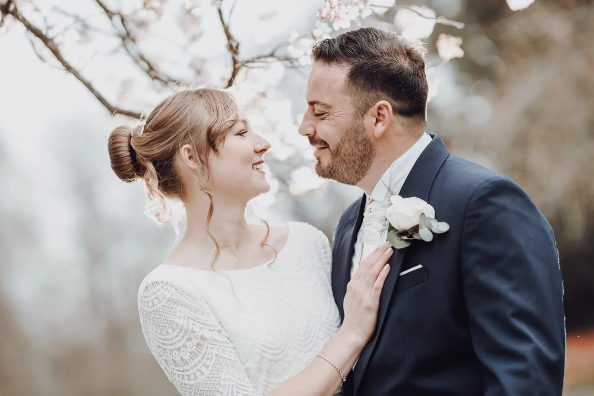 A bride and groom smiling under a cherry blossom tree.