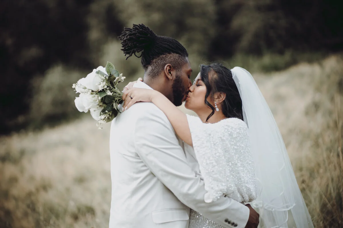 A bride and groom kissing in a field.