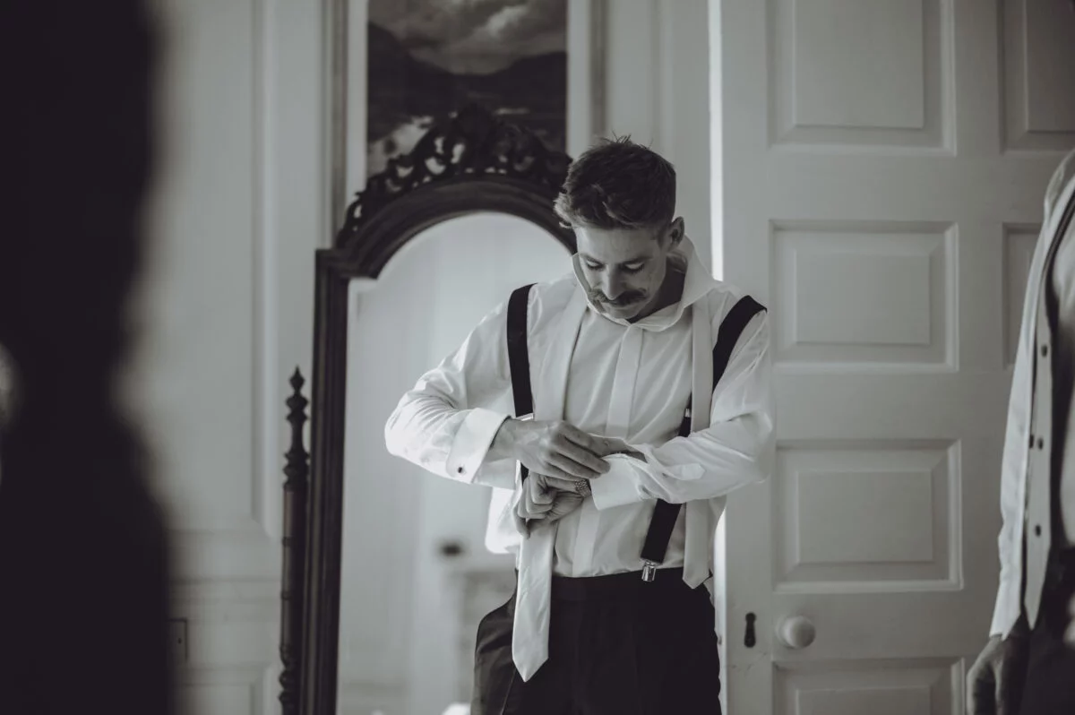 A man is adjusting his tie in front of a mirror.