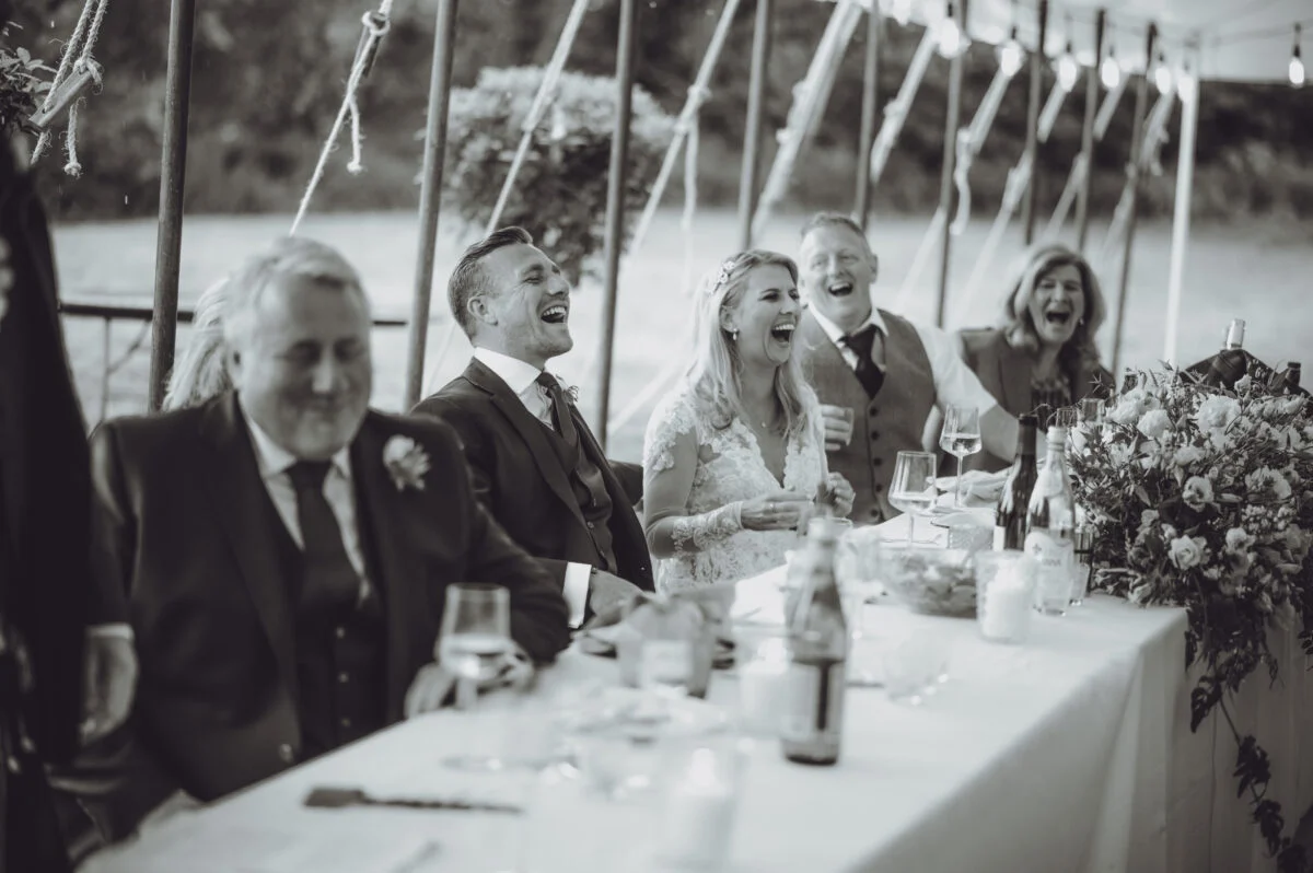 A black and white photo of a group of people laughing at a table.