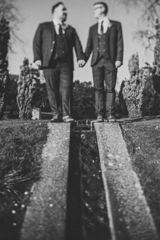 A black and white photo of two men holding hands in front of a fountain.
