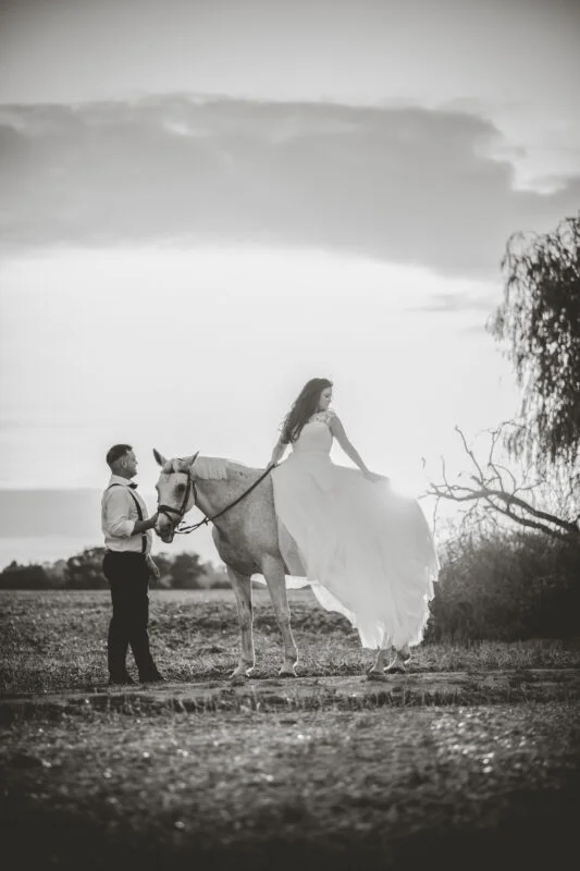 A bride and groom riding a horse in a black and white photo.