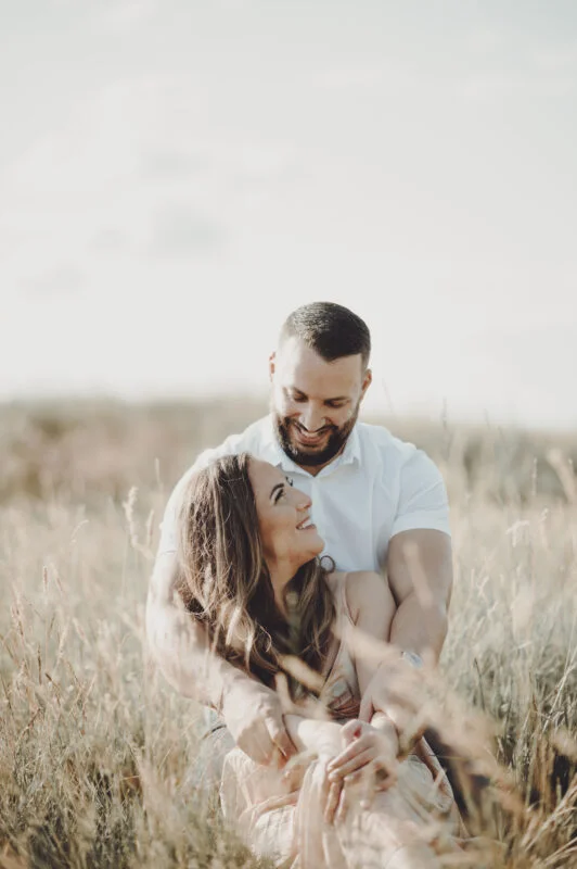 An engaged couple sitting in tall grass during their engagement session.