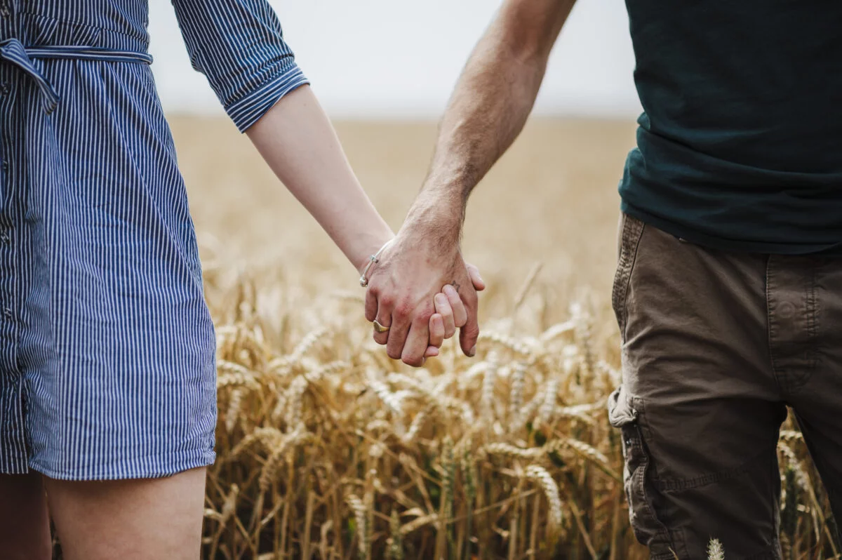 A man and woman holding hands in a wheat field.