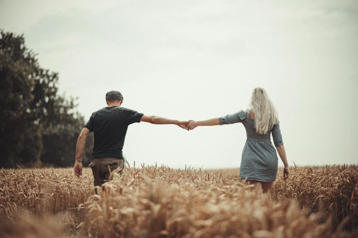 A man and woman holding hands in a wheat field.
