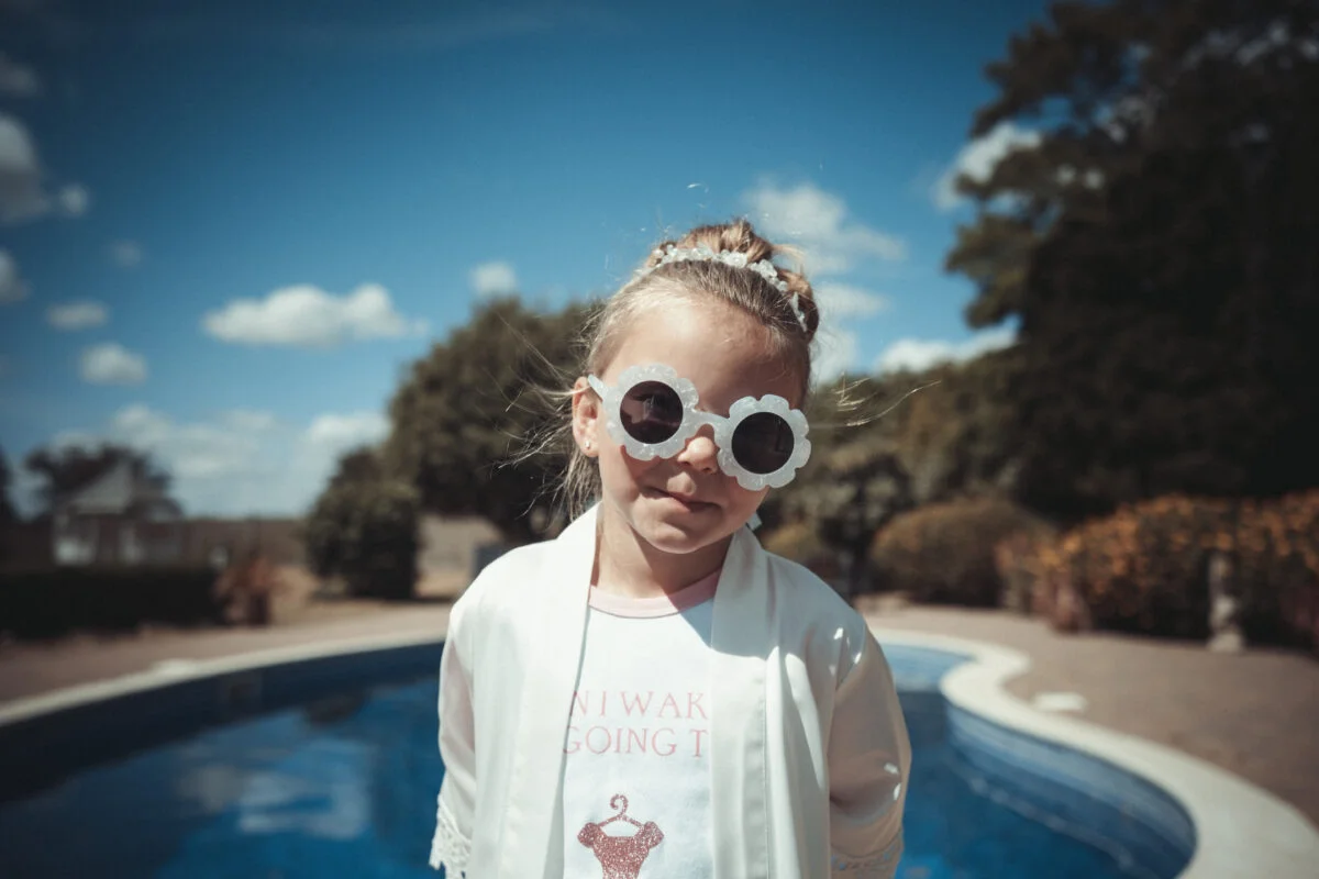 A little girl wearing sunglasses in front of a pool.