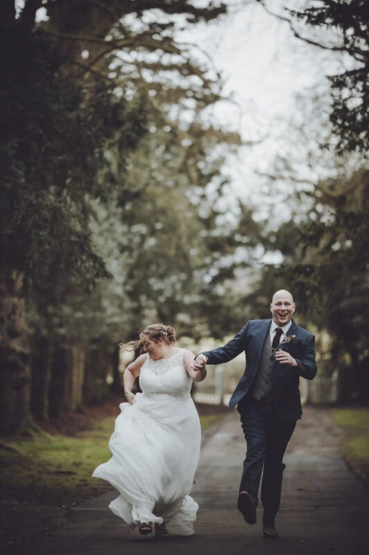 A bride and groom running down a path in the woods.