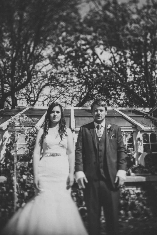 A bride and groom standing in front of a greenhouse.