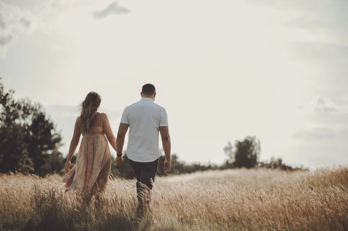 A couple walking through a field holding hands.