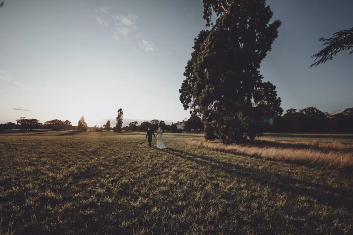 A bride and groom standing in a field at sunset.