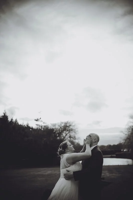A bride and groom kissing in front of a lake.