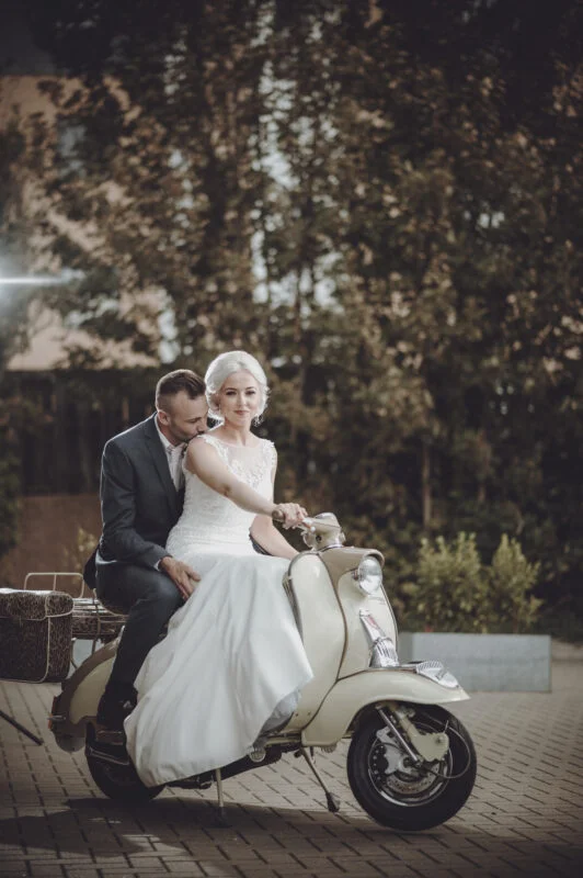 A bride and groom sitting on a vespa.