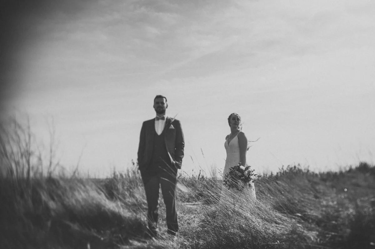 A bride and groom standing in a field of tall grass.