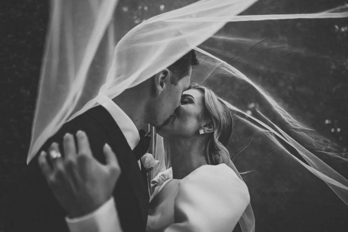 A bride and groom kiss under a veil.