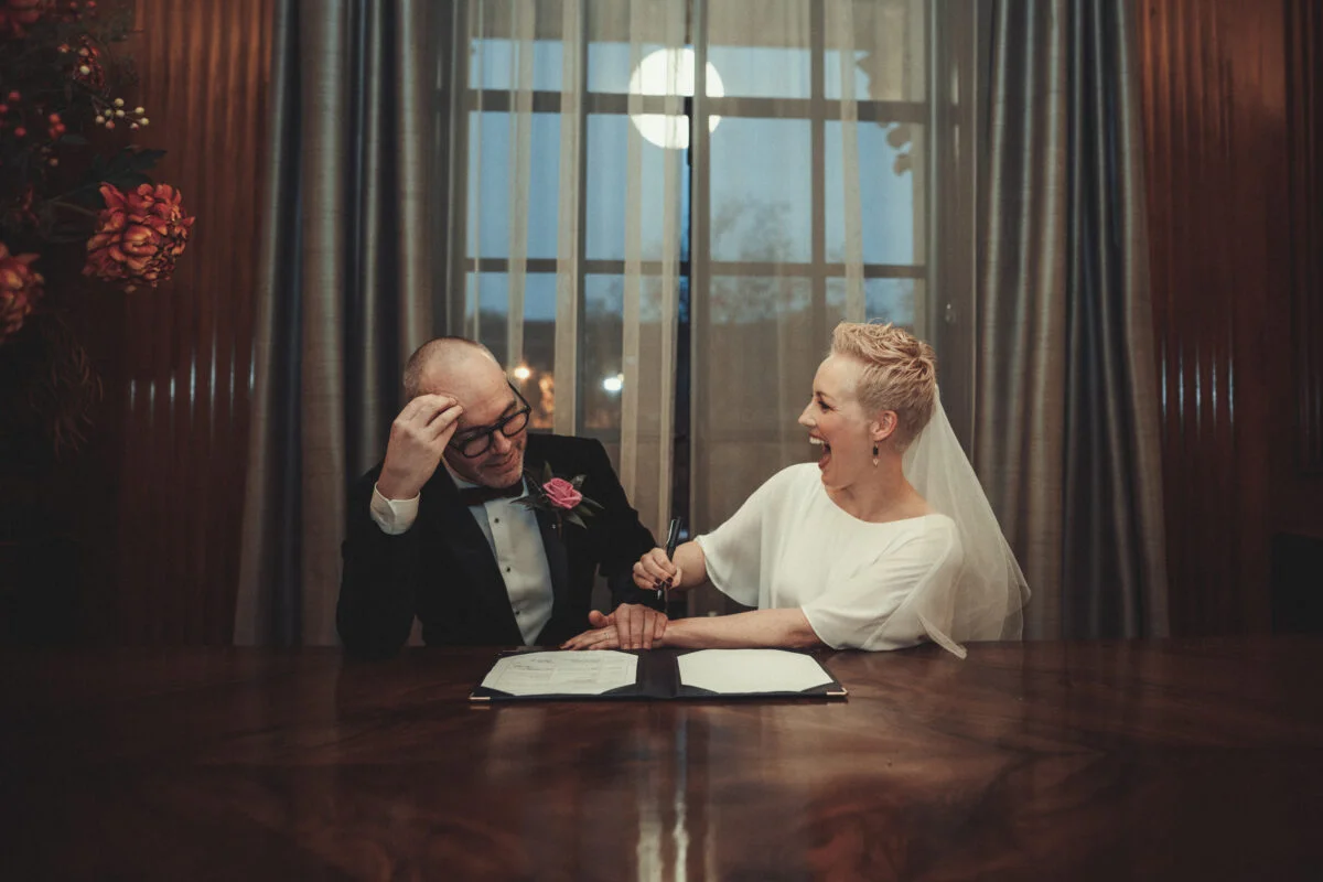 A bride and groom signing their wedding vows at a table.
