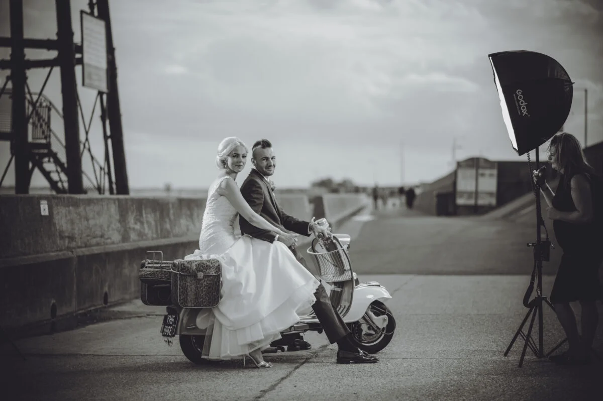A bride and groom on a scooter in front of a building.