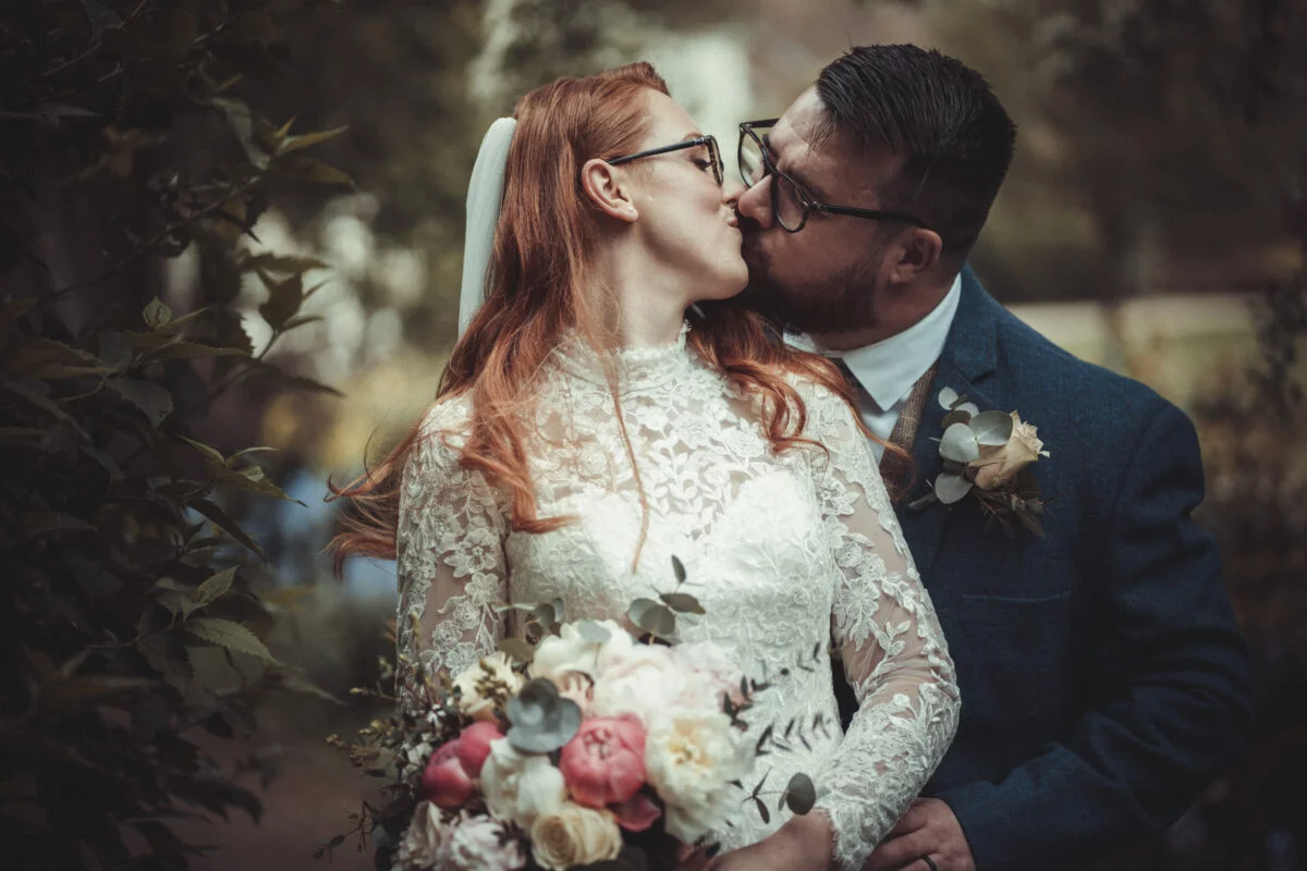 A bride and groom kissing in a garden.