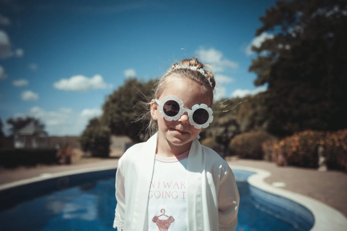 A little girl wearing sunglasses in front of a pool.