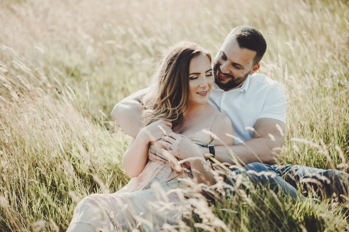 An engaged couple sitting in tall grass during their engagement session.