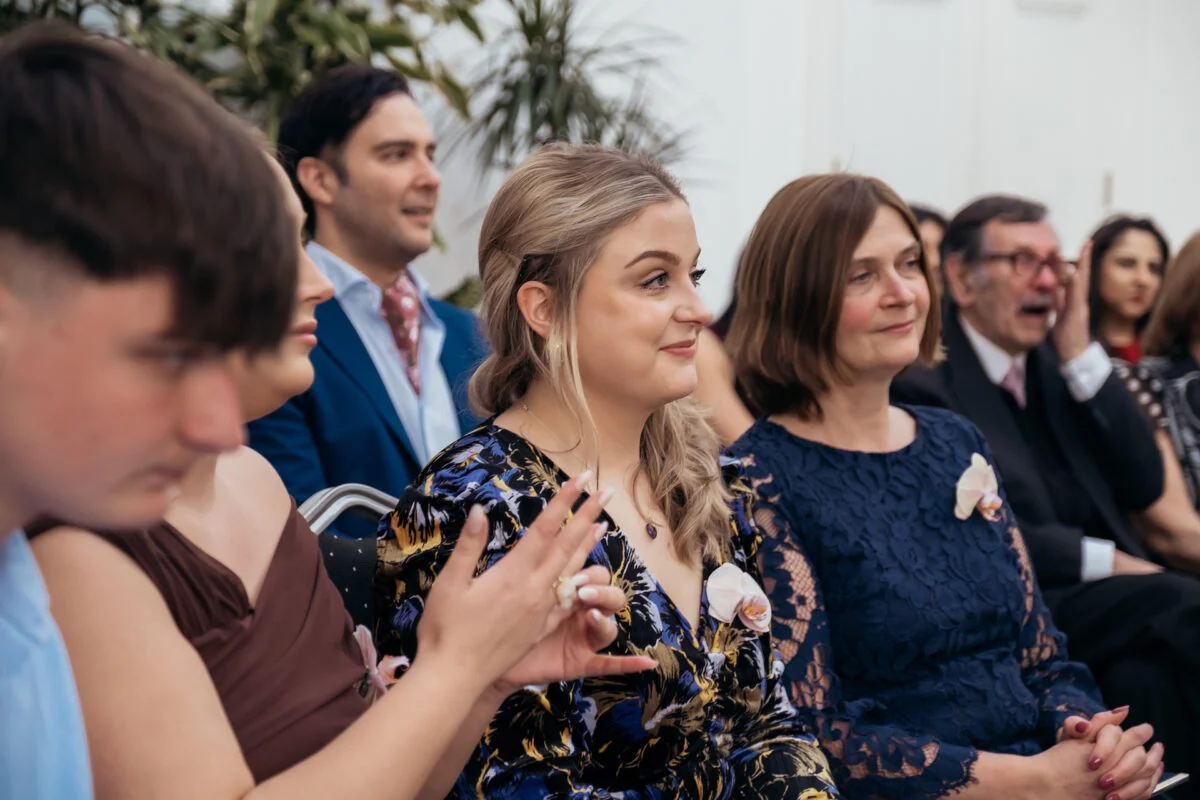 Wedding guests seated together smile and clap candidly during the ceremony celebrations.