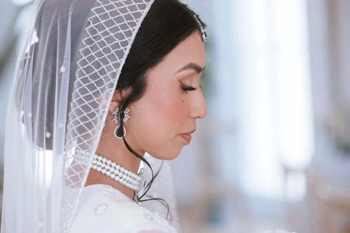 An exquisite profile portrait of a south asian bride adorned with a pearl-detailed veil and statement emerald drop earrings.