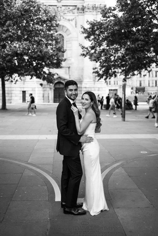 A newlywed couple poses together in a city square during their black and white wedding portrait session.