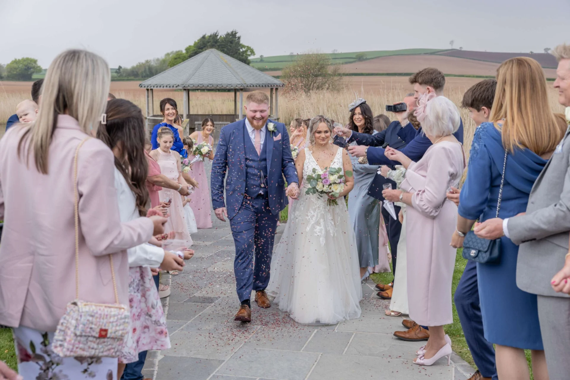 The newlyweds happily walk down an outdoor stone pathway hand in hand as guests shower them with colorful confetti petals.