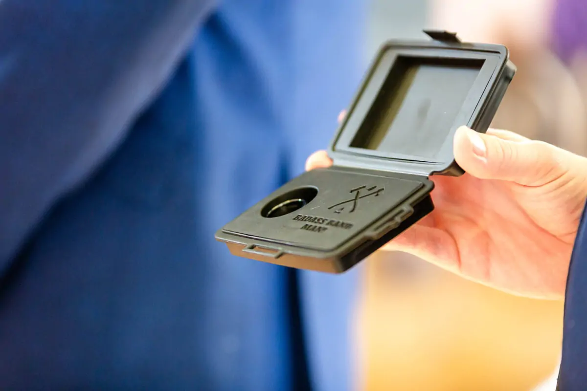 A close-up shot of a person holding an open black ring box containing a wedding band.
