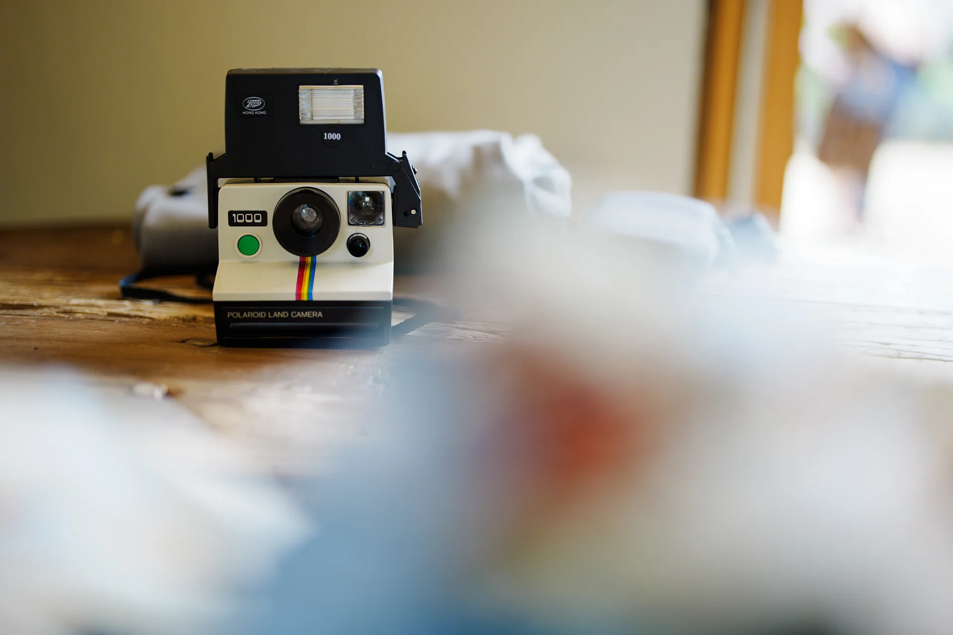 A vintage polaroid land camera sits on a wooden surface with a soft, blurred foreground.