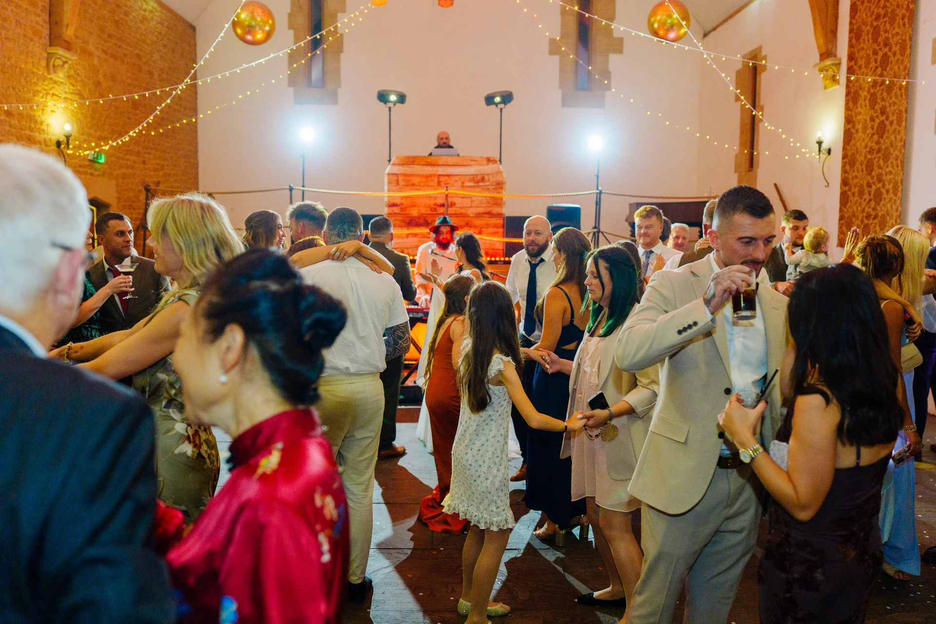 Guests enjoy the evening reception on a lively dance floor inside a rustic stone barn illuminated by hanging string lights.
