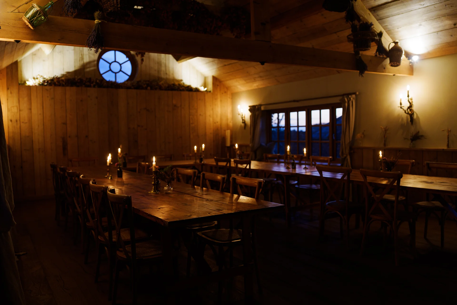 An atmospheric candlelit wedding reception setup in a rustic wooden barn featuring long banquet tables and exposed beams.