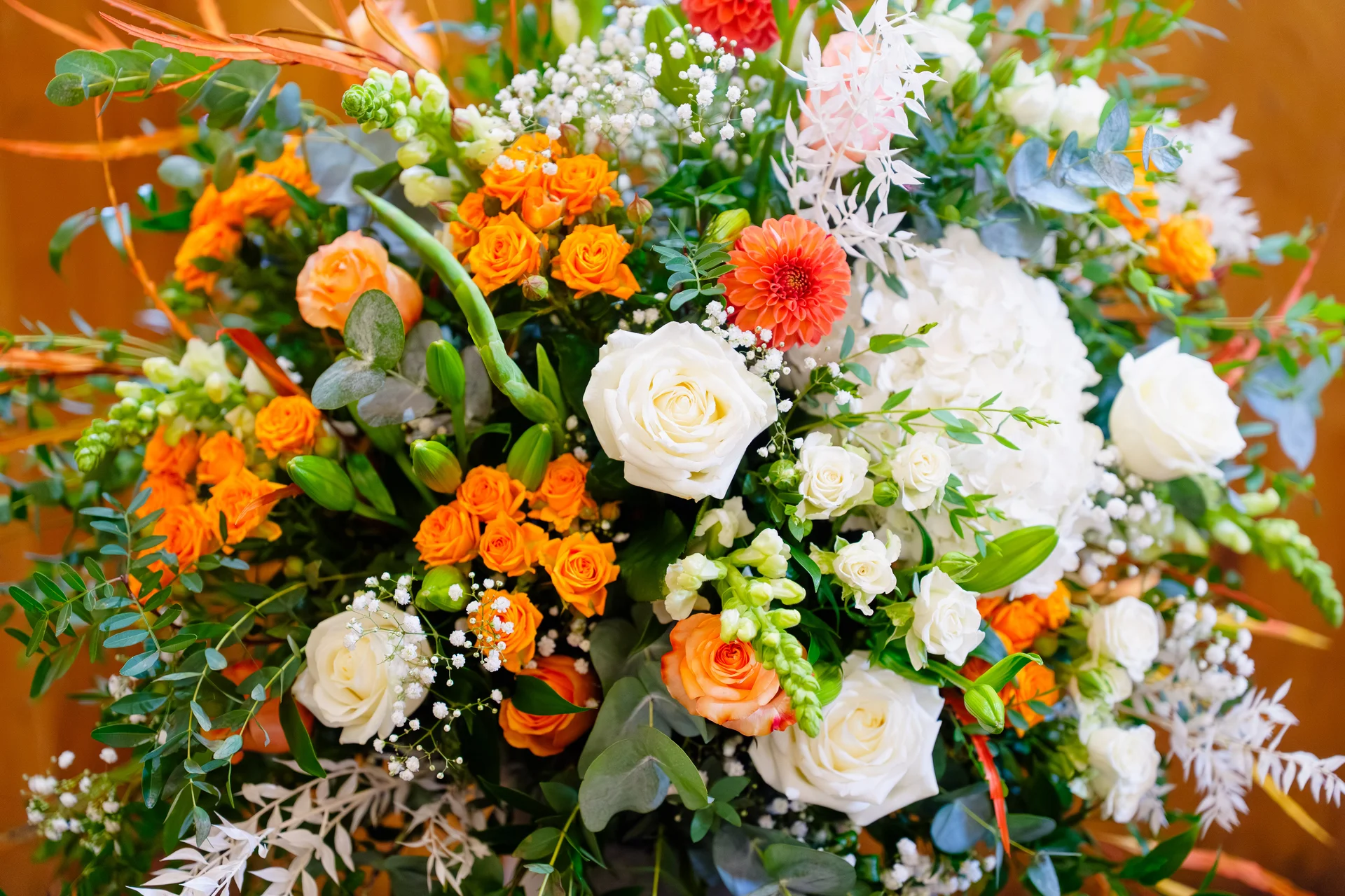 A vibrant wedding floral arrangement featuring white roses, orange spray roses, hydrangeas, and delicate greenery.
