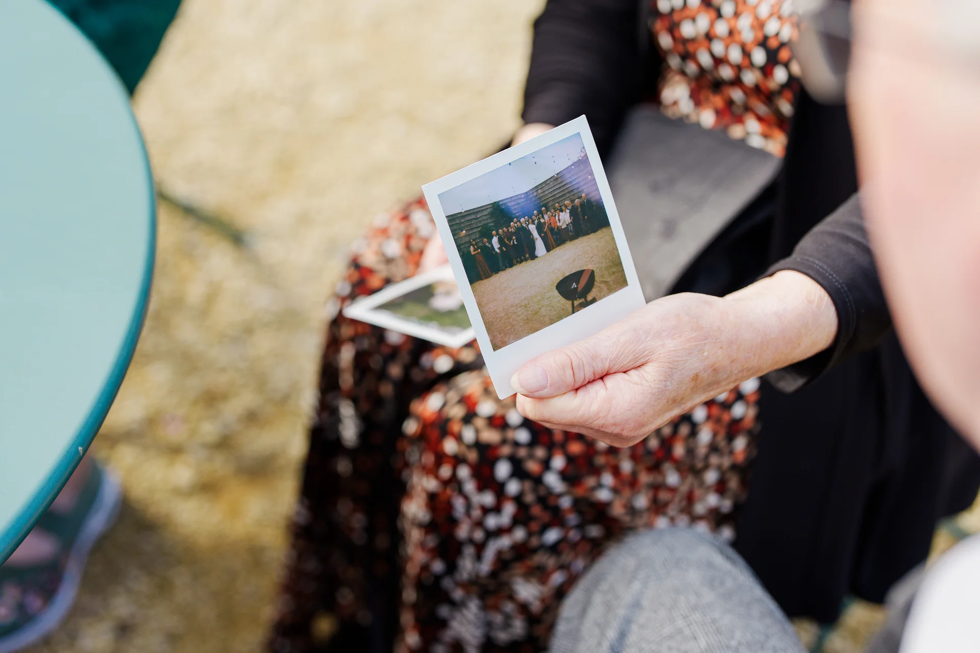 A guest holds up an instant polaroid photograph showing a group wedding portrait during the celebrations.