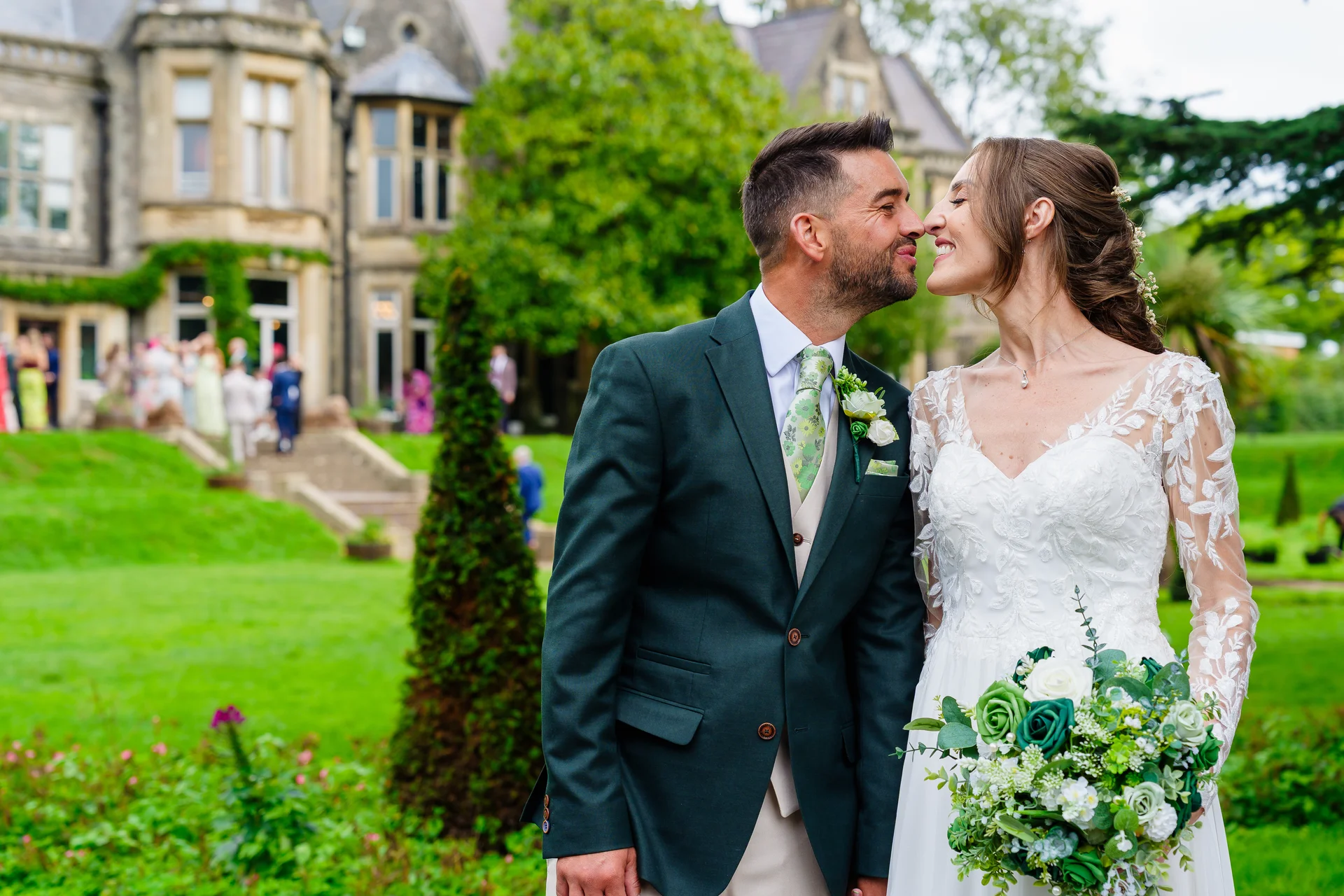 A bride and groom share a tender nose-to-nose moment in the manicured gardens of a historic country house venue.