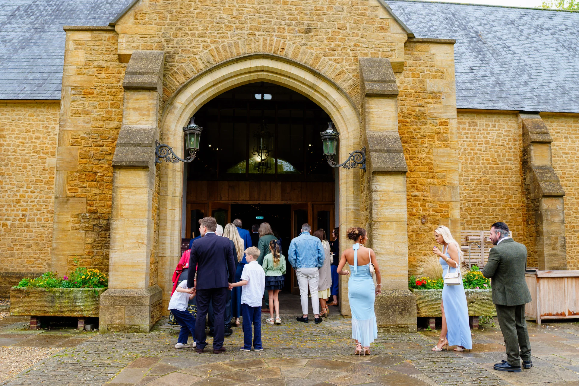 Wedding guests gather outside the striking stone archway entrance of a rustic barn venue.