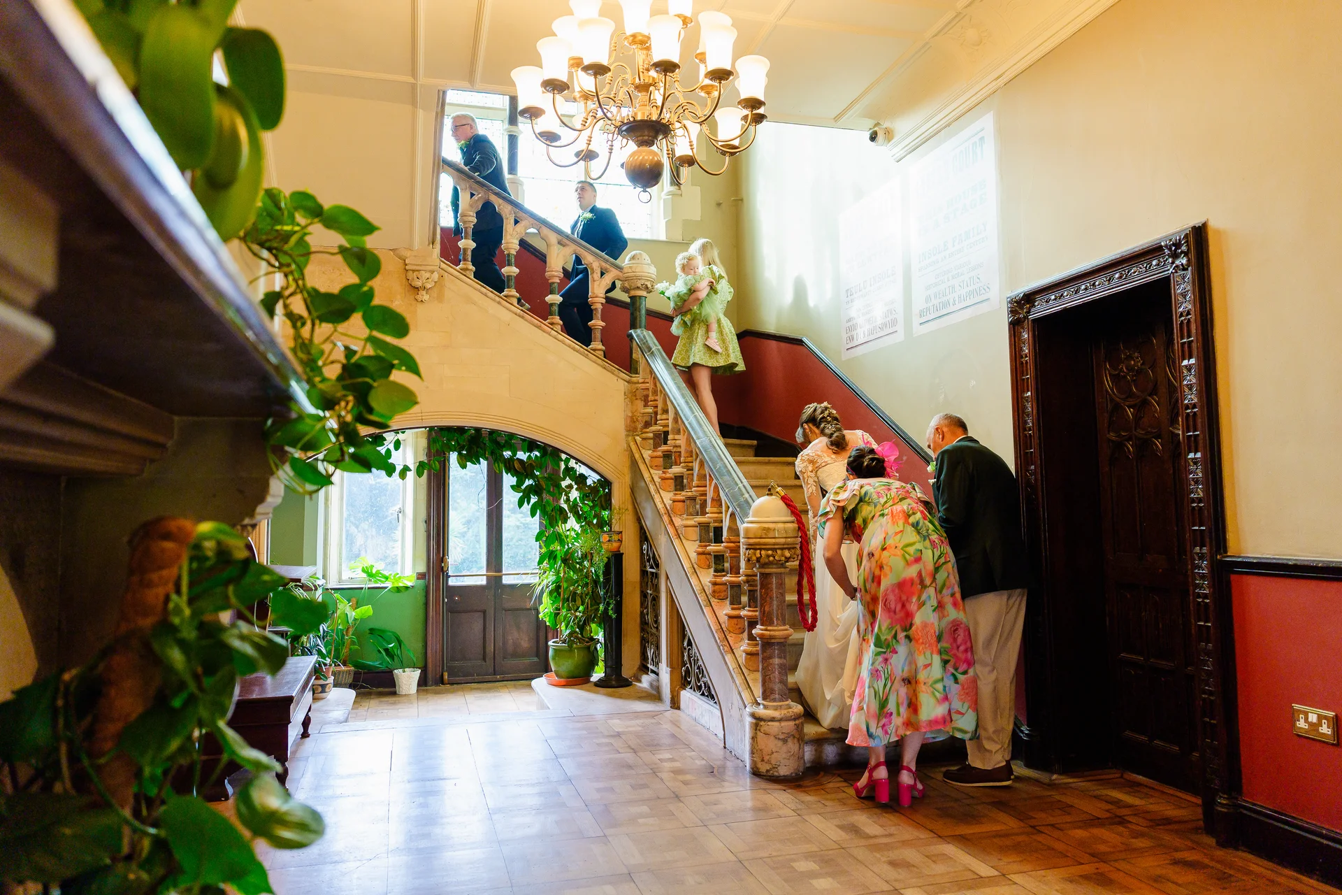 Guests and wedding party members ascend the grand wooden staircase inside a historic country house venue.