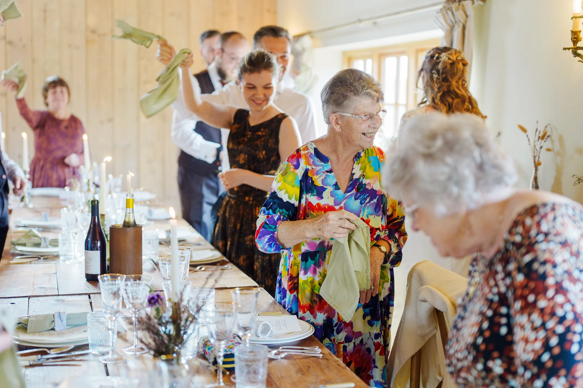 Joyful wedding guests wave their napkins in the air during a lively reception at a rustic wooden venue.
