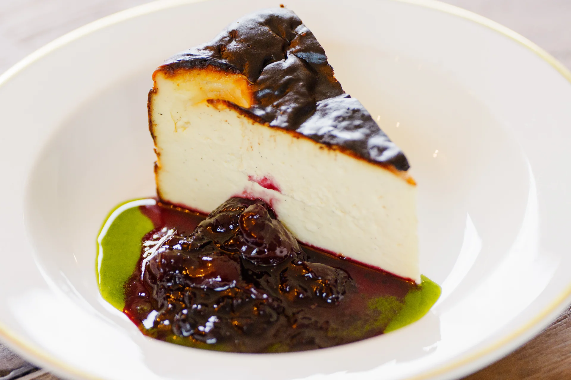A beautifully plated slice of burnt Basque cheesecake with berry compote and green coulis rests on a white dish for a wedding breakfast.