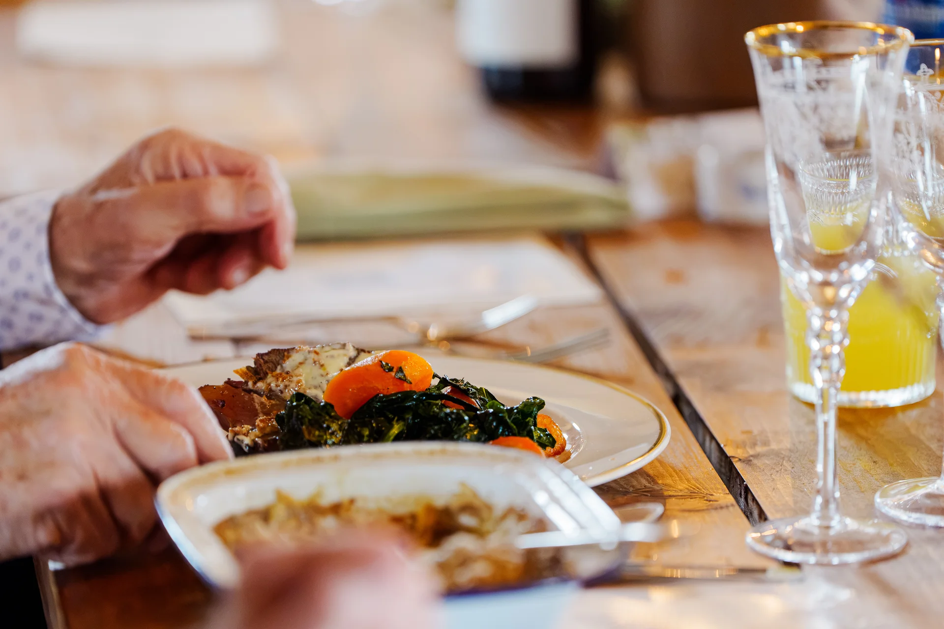 A guest enjoys a plated wedding breakfast featuring roasted meat and vegetables at a long wooden banquet table.