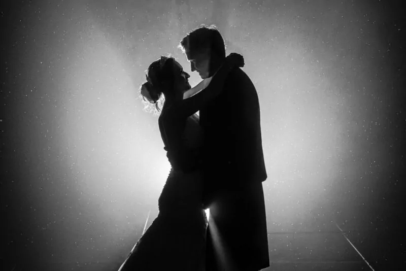 A dramatic black and white silhouette of a bride and groom embracing under a starry night sky with atmospheric backlighting.