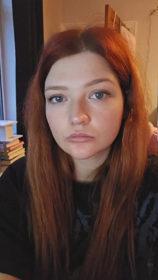 Close up portrait of a woman with long red hair and blue eyes looking directly towards the camera in natural indoor lighting.
